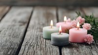Spa candles in pastel colors burning on rustic wooden surface with pink flowers creating peaceful wellness atmosphere for relaxation and meditation.