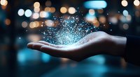 Magical glowing blue particles floating above open palm against blurred city lights background, representing innovation, technology and supernatural power.