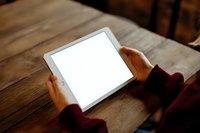 Person holding blank white screen tablet computer on wooden table for digital mockup and app presentation purposes.