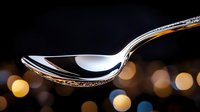 Elegant silver spoon on dark background with soft golden bokeh lights creating luxurious dining atmosphere, perfect for restaurant and culinary concepts.