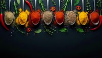 Colorful spices and herbs in wooden spoons arranged on dark background with fresh herbs, chili peppers and tomatoes for culinary cooking and seasoning.