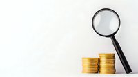 Magnifying glass examining stacks of golden coins on white background, financial analysis and investment research concept for business and economy.