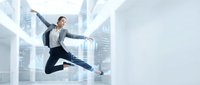 Young professional woman jumping with joy in modern office building celebrating business success and achievement.