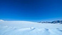 Vast snowy landscape with rolling white drifts under clear blue sky and distant snow-capped mountains, suitable for winter backgrounds and nature themes.