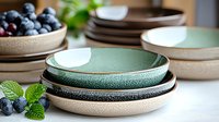 Handcrafted ceramic bowls in mint green and natural beige tones with textured finish, stacked on table with fresh blueberries and mint leaves, food photography.
