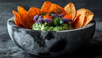Fresh guacamole dip with colorful edible flowers served in stone molcajete bowl with crispy tortilla chips for Mexican cuisine and appetizer presentations.