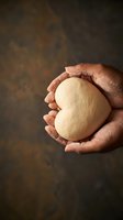 Hands holding fresh bread dough ball ready for baking on rustic wooden surface with flour dust creating warm homemade cooking atmosphere.