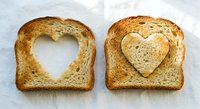 Two slices of toasted bread with heart-shaped cutouts on white background, perfect for romantic breakfast concepts and love-themed food photography.