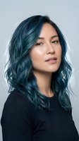 Young Asian woman with vibrant teal blue dyed hair wearing black top against gray background. Modern hair color transformation and styling concept.
