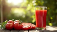 Fresh tomato juice in glass with ripe red tomatoes on wooden table in sunny garden setting for healthy lifestyle and nutrition concepts.