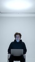 Young Caucasian male programmer working late on laptop in minimalist white office space with blue screen light reflection on face creating modern workspace atmosphere.