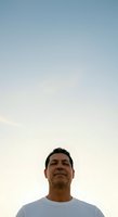 Middle-aged Hispanic male wearing casual white t-shirt, looking upward against clear sky backdrop during golden hour, conveying contemplation and hope for advertising and lifestyle campaigns.