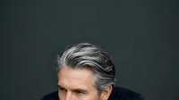 Mature man with gray and white hair, caucasian ethnicity, wearing dark clothing against neutral background for corporate or professional headshot use.