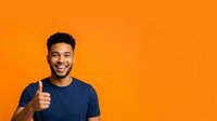 Young man with dark curly hair and medium brown skin tone wearing navy t-shirt giving thumbs up gesture against bright orange background, expressing approval and positivity for advertising and marketing campaigns.