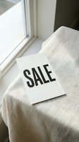 Sale sign card resting on linen fabric near a bright window, minimal style for retail, fashion, and seasonal discount promotions.