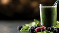 Fresh green smoothie with spinach leaves, blackberries and raspberries on dark background. Healthy detox drink with berries and leafy greens.