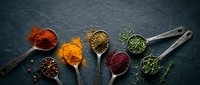 Colorful spices and herbs arranged in vintage metal spoons on dark slate background. Culinary ingredients for cooking and seasoning food preparation.