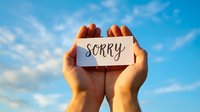 Hands holding white card with sorry message against blue sky with clouds. Apology concept for forgiveness, reconciliation and emotional healing communication.