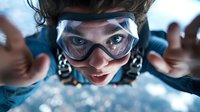Skydiver wearing protective goggles falling through clouds during freefall, capturing intense aerial action with dramatic perspective and adrenaline-filled expression.