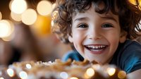 Joyful young child with curly hair and bright smile against warm bokeh lights background, expressing pure happiness and genuine emotion.