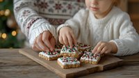 Child decorating Christmas cookies with colorful sprinkles on wooden board, wearing cozy white sweater in festive holiday setting.