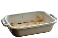 Empty ceramic baking dish with food residue and stains after cooking, showing signs of use with brown spots and crumbs on white interior surface.