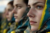 Young women wearing traditional headscarves in blue and yellow colors stand in line, faces showing determination and strength. Close-up portrait captures cultural heritage.