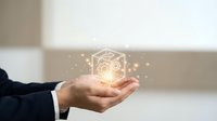 Businessman hand holding glowing cube with gear mechanism and sparkles representing innovation technology and digital transformation concepts.
