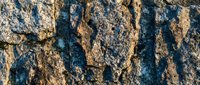 Rough textured rock surface with deep cracks and crevices showing natural weathering patterns and geological formations for backgrounds and textures.