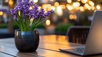 Purple hyacinths in black ceramic pot on wooden table with laptop and bokeh lights creating cozy evening atmosphere for remote work or studying.