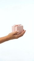 Female hand holding pink gift box with ribbon bow isolated on white background for holiday celebrations and special occasions.