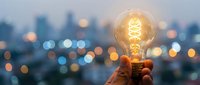 Hand holding glowing vintage light bulb against blurred city lights at dusk, symbolizing innovation, creativity and bright ideas for business success.