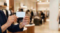 Businessman holding blank white card in retail store environment with blurred shopping background for branding and marketing purposes.