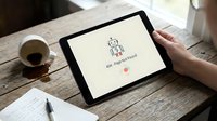 Person holding tablet displaying app interface with robot icon and loading message on wooden desk with coffee cup and notebook.