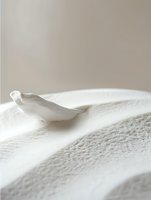 White feather resting on soft textured fabric creates minimalist composition with gentle shadows and light, expressing purity and tranquility in neutral tones.
