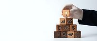 Business professional hand placing wooden cube with growth chart icon on pyramid stack of blocks with financial and business symbols for strategic planning.