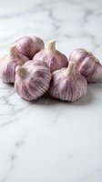 Fresh purple garlic bulbs arranged on white marble surface for culinary cooking and healthy organic food preparation in modern kitchen setting.