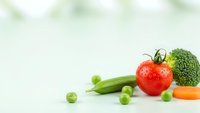 Fresh organic vegetables including ripe red tomato, green peas, broccoli and carrot arranged on clean white surface for healthy cooking and nutrition.
