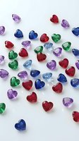 Colorful heart-shaped gemstones in red, blue, green and purple scattered on white background for jewelry design and romantic decorations.