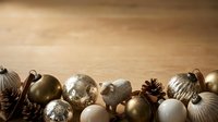 Festive holiday ornaments in metallic gold, silver, and white tones arranged on warm wooden surface for seasonal decorating and celebration themes.