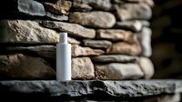 White cosmetic bottle on rustic stone shelf against natural rock wall background for skincare and beauty product mockup presentations.