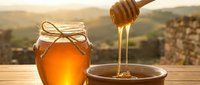 Golden honey dripping from wooden dipper into bowl with jar on rustic table against mountain landscape at sunset for natural organic food and wellness concepts.