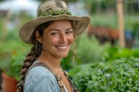 Young Hispanic woman gardener in sun hat and denim shirt smiling while working in lush greenhouse garden, perfect for agriculture, farming and organic lifestyle advertising.