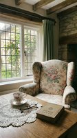 Cozy cottage interior with floral armchair by window, exposed beams, stone walls, teacup and book on wooden table creating peaceful reading nook atmosphere.
