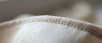 Close-up macro shot of beige fabric seam with detailed stitching thread texture for textile manufacturing and fashion design projects.