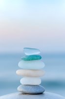 Stack of smooth sea glass and stones balanced on beach with soft pastel sky background creating zen meditation atmosphere for wellness concepts.