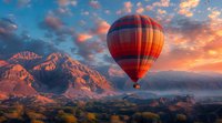 Hot air balloon floating over majestic mountain landscape at dramatic sunset with vibrant orange clouds and golden light illuminating rocky peaks, perfect for travel and adventure themes.