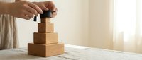 Hands placing a miniature graduation cap on top of stacked wooden blocks, symbolizing academic achievement, education milestones, and career growth.