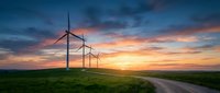 Wind turbines on green field at sunset with dramatic sky and rural road leading to renewable energy farm for sustainable power generation.