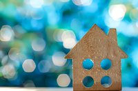 Wooden house cutout with circular windows against dreamy blue bokeh background for real estate and home concepts.